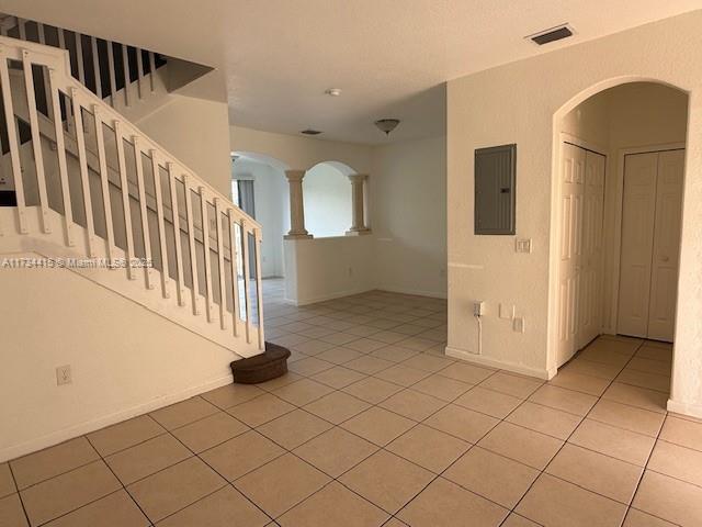 unfurnished room featuring light tile patterned floors, electric panel, visible vents, and arched walkways