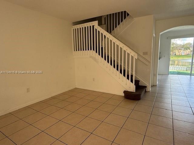 staircase featuring baseboards, arched walkways, and tile patterned floors