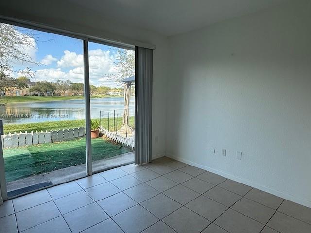 unfurnished room with a water view, baseboards, and light tile patterned flooring