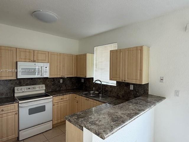 kitchen featuring dark countertops, white appliances, a peninsula, and a sink