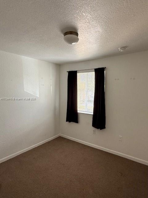 unfurnished room with a textured ceiling, dark carpet, and baseboards