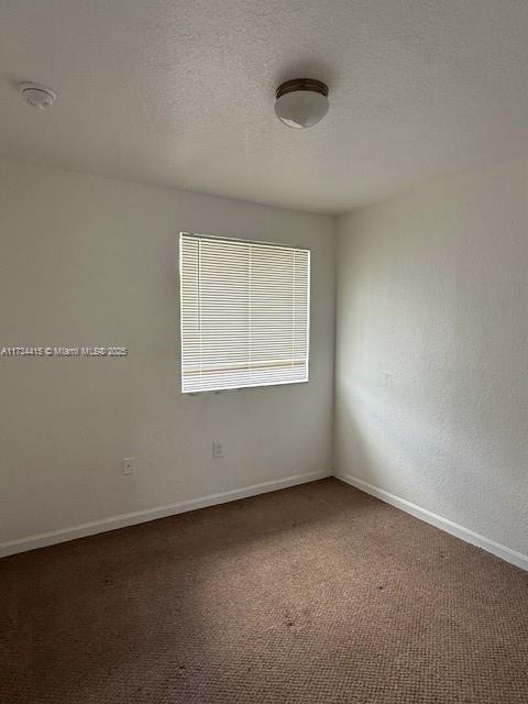 unfurnished room with a textured ceiling, dark carpet, and baseboards