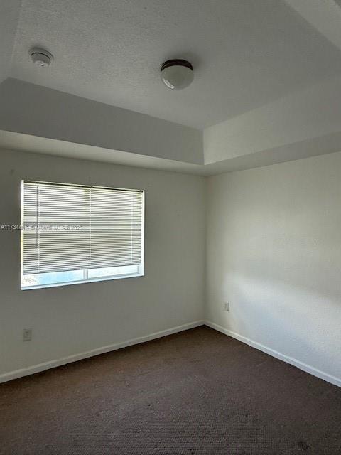 unfurnished room with a textured ceiling, dark colored carpet, and baseboards