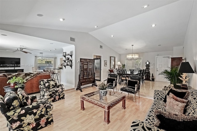 living room featuring lofted ceiling, ceiling fan with notable chandelier, and light wood-type flooring