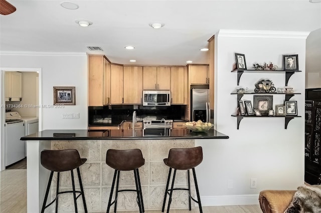 kitchen featuring appliances with stainless steel finishes, backsplash, ornamental molding, separate washer and dryer, and kitchen peninsula