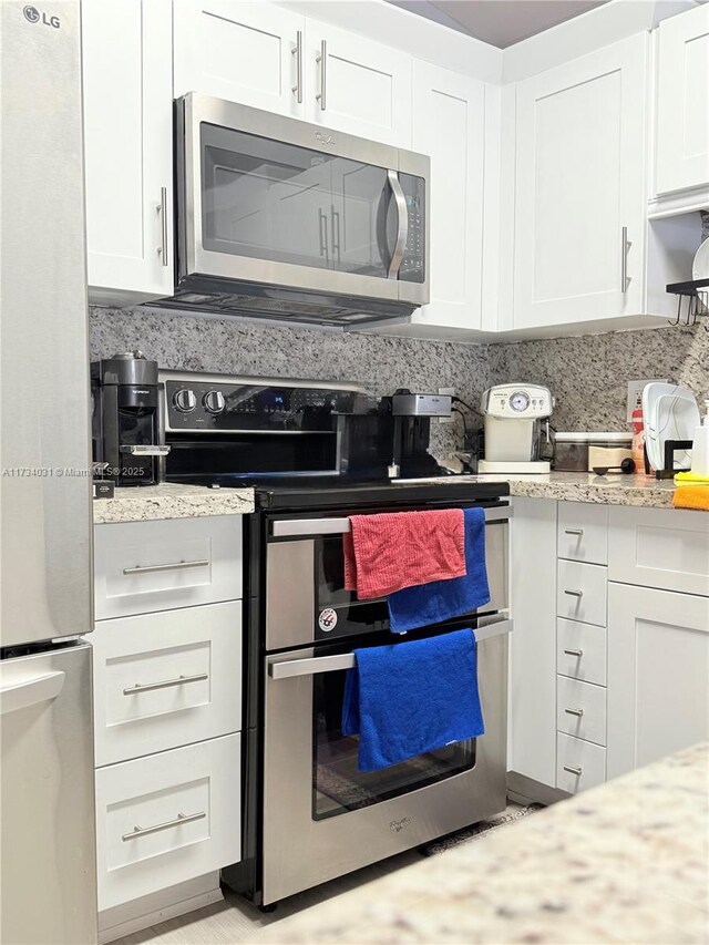 kitchen featuring backsplash, appliances with stainless steel finishes, light stone counters, and white cabinets