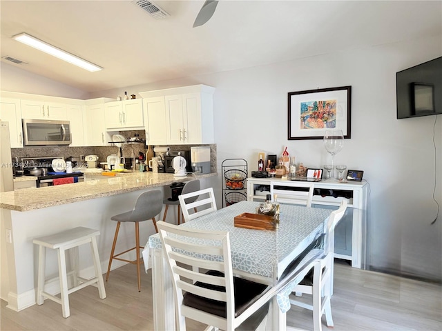 kitchen featuring appliances with stainless steel finishes, backsplash, a kitchen breakfast bar, light hardwood / wood-style floors, and white cabinets