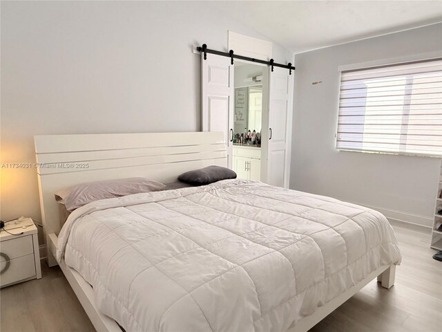 bedroom with a barn door, lofted ceiling, and light hardwood / wood-style flooring