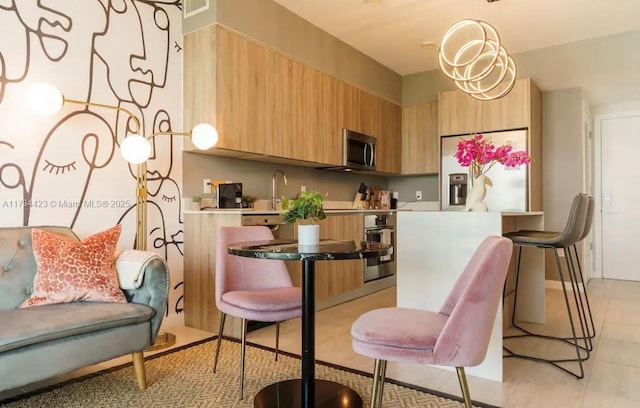 kitchen featuring pendant lighting, stainless steel appliances, light brown cabinetry, and sink