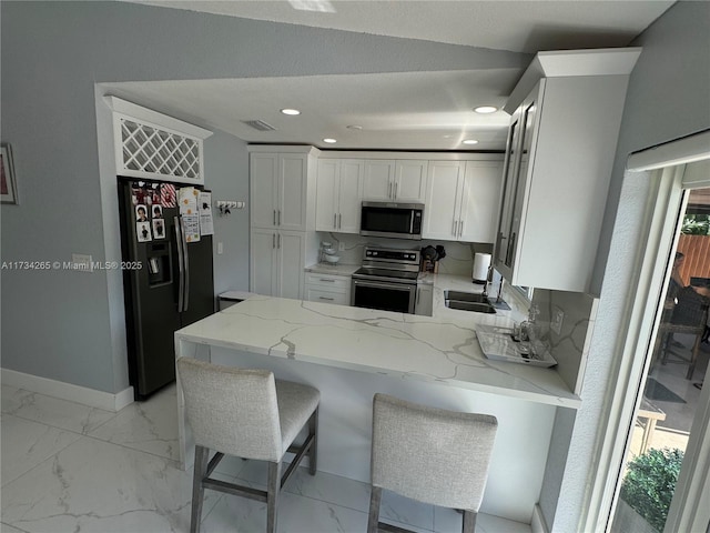 kitchen featuring light stone counters, a peninsula, a sink, stainless steel appliances, and marble finish floor