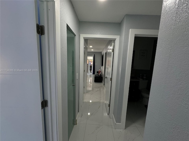 corridor with marble finish floor and a textured wall