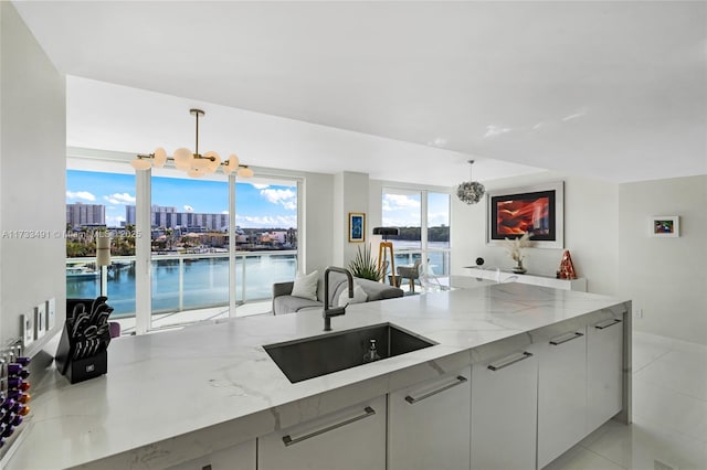 kitchen with a water view, light stone countertops, sink, and hanging light fixtures