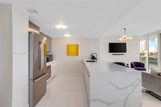 kitchen with sink, white cabinetry, light stone counters, decorative light fixtures, and stainless steel refrigerator