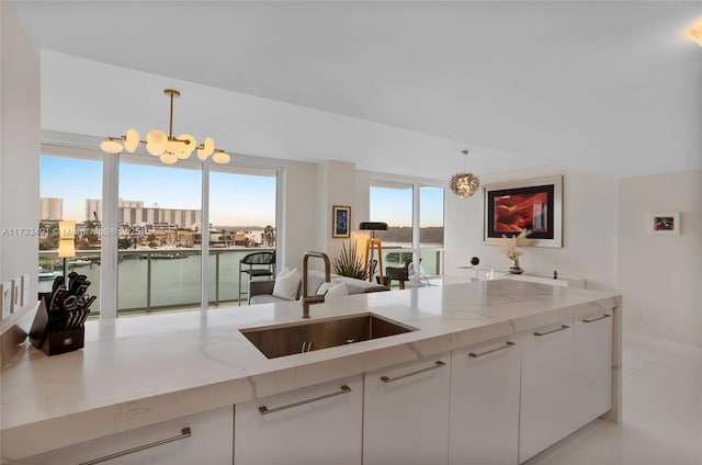 kitchen with sink, light stone countertops, hanging light fixtures, and white cabinets