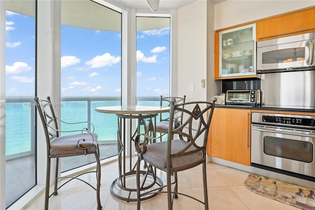 kitchen featuring a water view, a wall of windows, appliances with stainless steel finishes, and light tile patterned floors