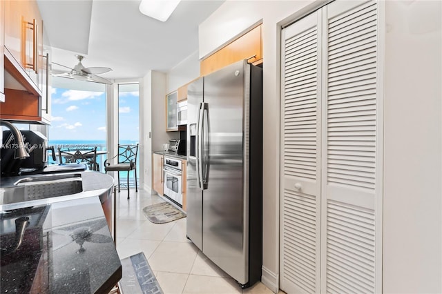 kitchen with appliances with stainless steel finishes, light tile patterned floors, ceiling fan, floor to ceiling windows, and a water view