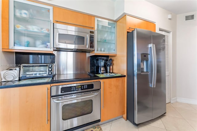 6365 Collins Ave Unit 1901, Miami Beach, FL 33141 - kitchen featuring appliances with stainless steel finishes, dark countertops, decorative backsplash, glass insert cabinets, and light tile patterned floors
