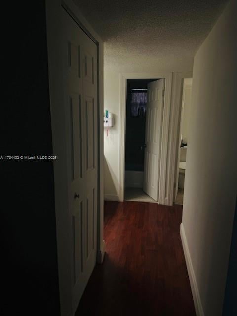 corridor featuring a textured ceiling, wood finished floors, and baseboards