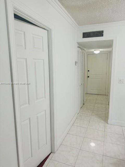 hall with a textured ceiling, light tile patterned flooring, visible vents, baseboards, and ornamental molding