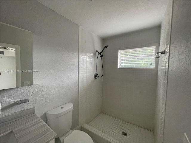 bathroom with toilet, a textured ceiling, and a tile shower