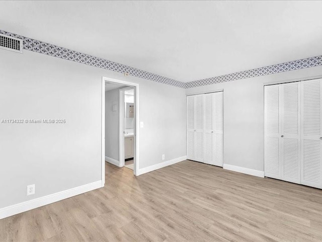 unfurnished bedroom with two closets and light wood-type flooring