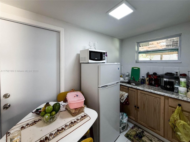 kitchen with light stone counters, light tile patterned floors, and fridge