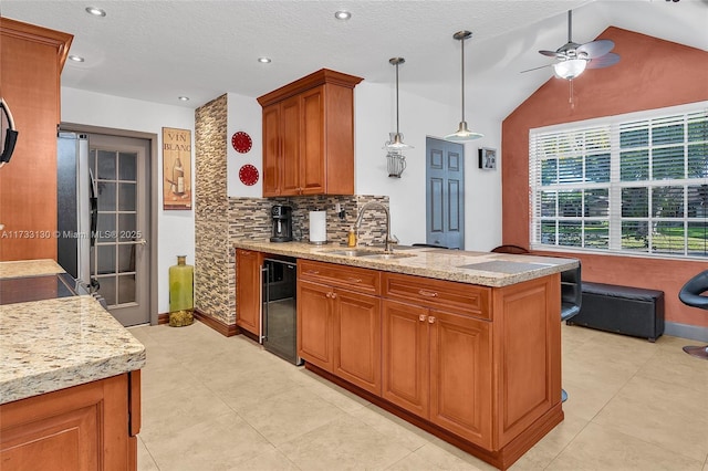 kitchen featuring pendant lighting, vaulted ceiling, sink, and light stone counters