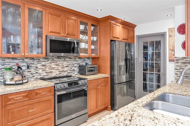 kitchen featuring light stone counters, appliances with stainless steel finishes, sink, and backsplash