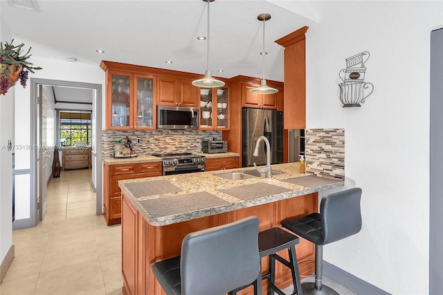 kitchen featuring sink, kitchen peninsula, stainless steel appliances, light stone countertops, and decorative backsplash