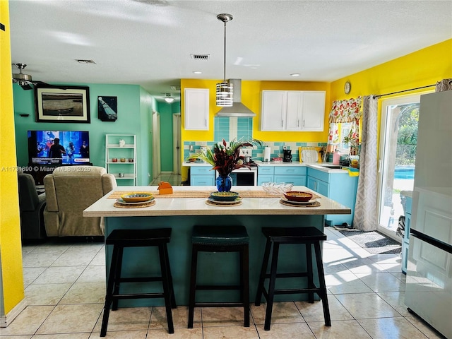 kitchen featuring pendant lighting, white cabinets, a kitchen breakfast bar, and wall chimney exhaust hood