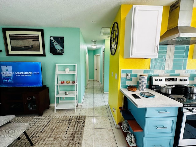 kitchen with white cabinetry, decorative backsplash, stainless steel range with electric stovetop, light tile patterned floors, and wall chimney range hood