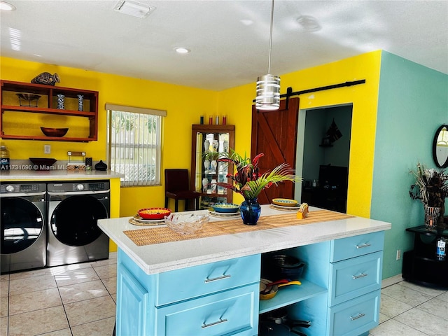 kitchen with light tile patterned floors, blue cabinetry, washing machine and dryer, decorative light fixtures, and a barn door