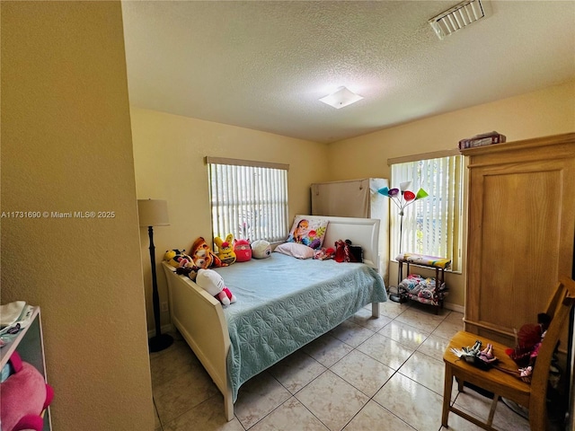 bedroom featuring multiple windows, light tile patterned floors, and a textured ceiling