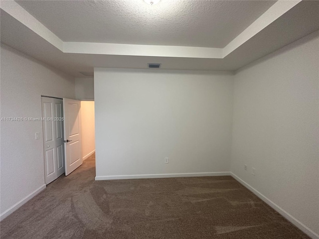 carpeted empty room featuring a tray ceiling and a textured ceiling