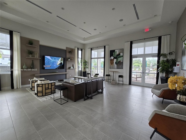 living room with french doors, a tray ceiling, light tile patterned flooring, and a wealth of natural light