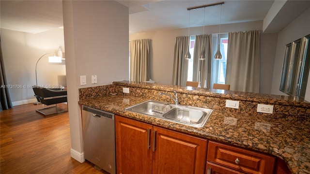 kitchen featuring brown cabinetry, dark stone counters, a sink, dark wood-type flooring, and stainless steel dishwasher