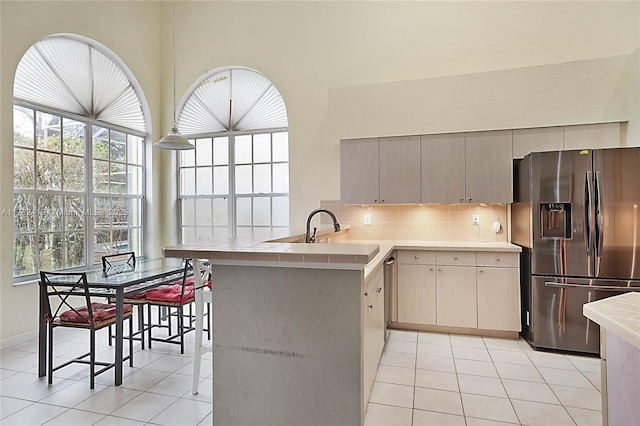 kitchen with light tile patterned flooring, tile counters, kitchen peninsula, stainless steel appliances, and decorative backsplash