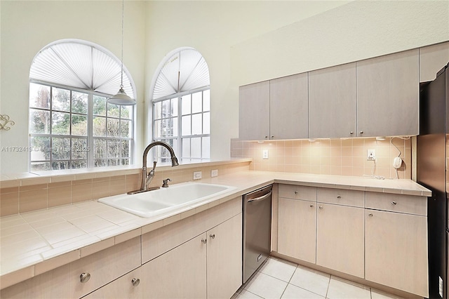 kitchen with sink, black refrigerator, backsplash, tile counters, and stainless steel dishwasher