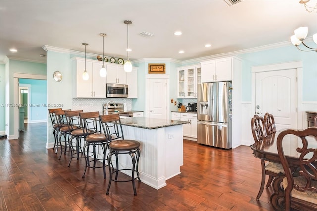 kitchen featuring a peninsula, dark wood-type flooring, appliances with stainless steel finishes, a kitchen bar, and glass insert cabinets