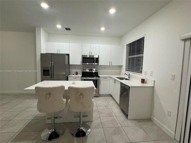 kitchen featuring light tile patterned flooring, appliances with stainless steel finishes, sink, a breakfast bar area, and white cabinets