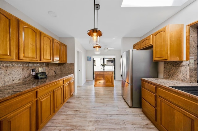 kitchen featuring tasteful backsplash, decorative light fixtures, a skylight, and stainless steel refrigerator