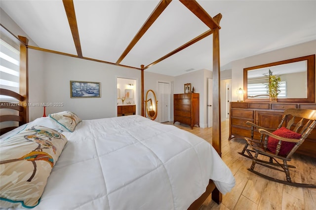 bedroom with ensuite bathroom, light wood-type flooring, and a closet