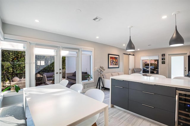 kitchen with decorative light fixtures, wine cooler, a center island, a barn door, and light hardwood / wood-style flooring