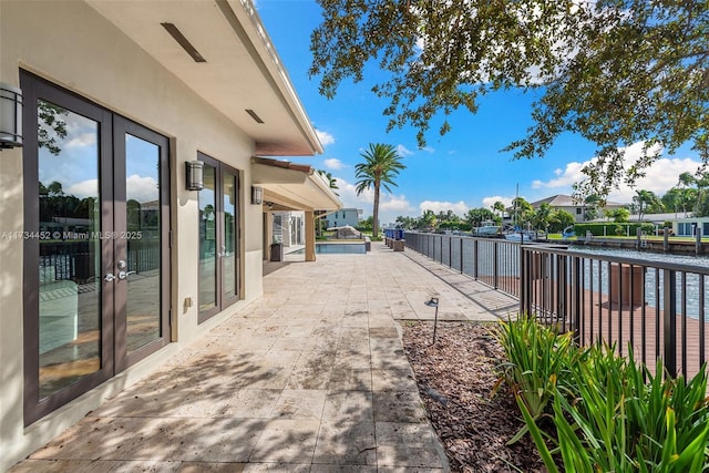 view of patio / terrace featuring a water view, fence, and french doors