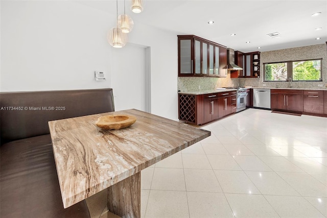 kitchen featuring light tile patterned floors, decorative backsplash, wall chimney exhaust hood, appliances with stainless steel finishes, and a sink