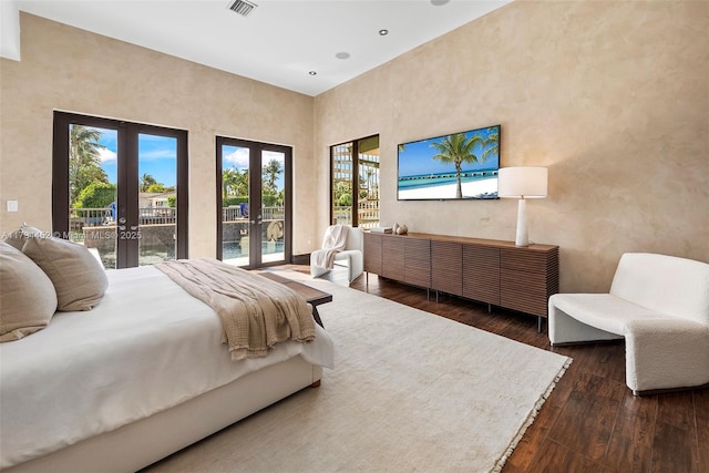 bedroom with a towering ceiling, hardwood / wood-style flooring, access to outside, and french doors