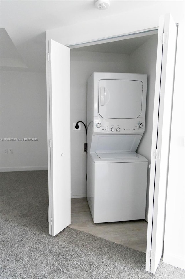 laundry area with light colored carpet and stacked washer / drying machine