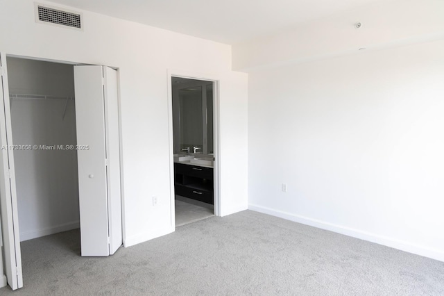 unfurnished bedroom featuring light carpet, a closet, and ensuite bathroom