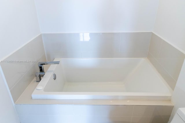 bathroom with toilet and tiled tub