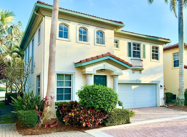 mediterranean / spanish house with a tiled roof, decorative driveway, an attached garage, and stucco siding